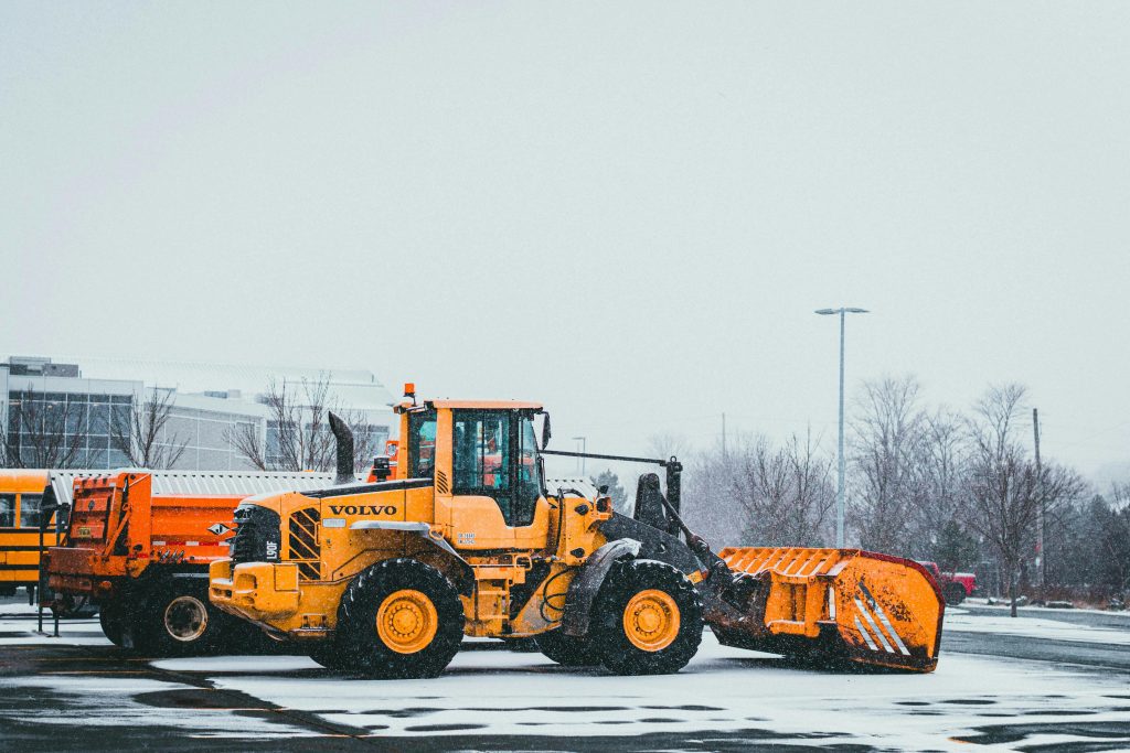 A yellow bulldozer by Volvo clearing snow in a winter landscape. Industrial machinery for snow removal.