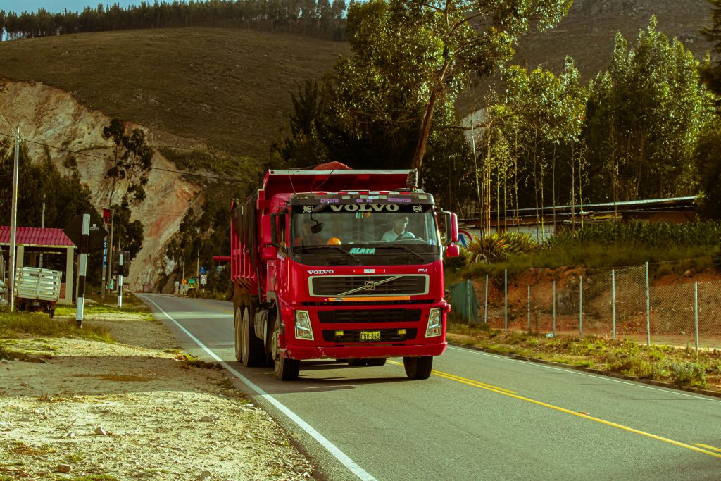 Red truck traveling on a scenic road with mountains and greenery, offering a sense of adventure.